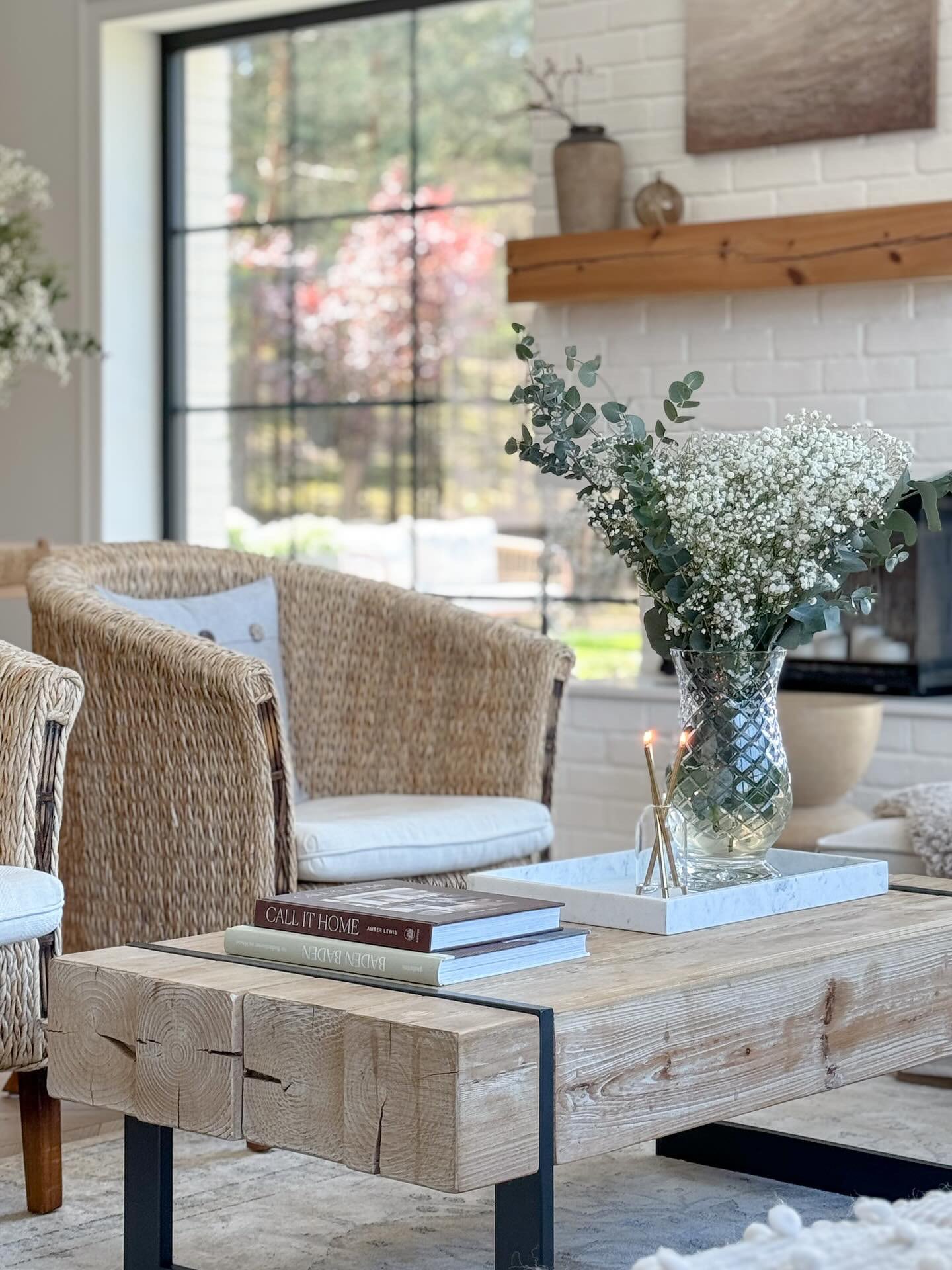 Drewniany stół z pięknymi białymi kwiatami i świeca oliensa gold crystal. Słoneczny dzień, wiklinowe fotele i styl modern farmhouse