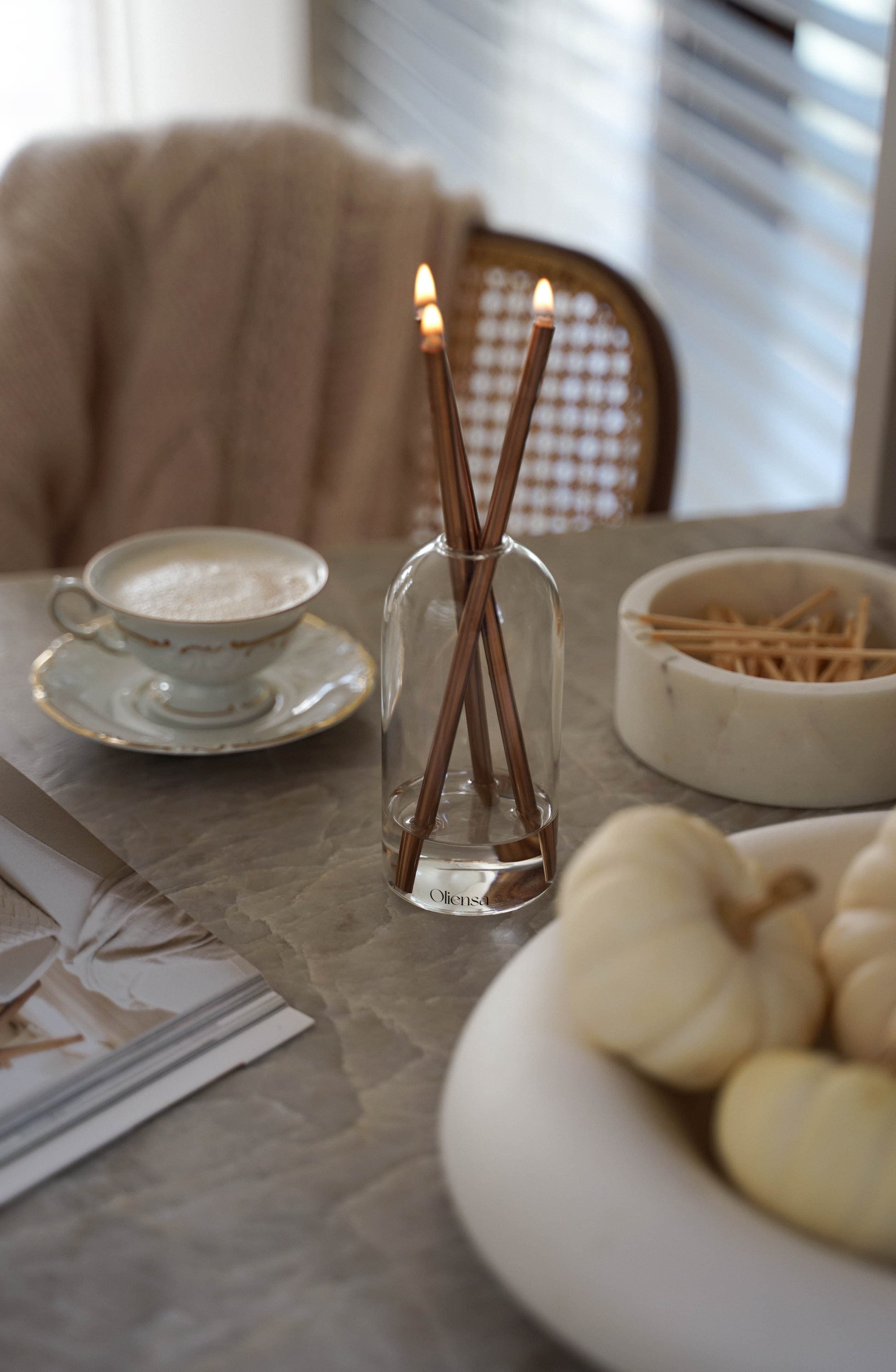 Filiżanka kawy w porcelanowej filiżance w towarzystwie delikatnych płomieni świecy Oliensa Eternal Copper Crystal. 
