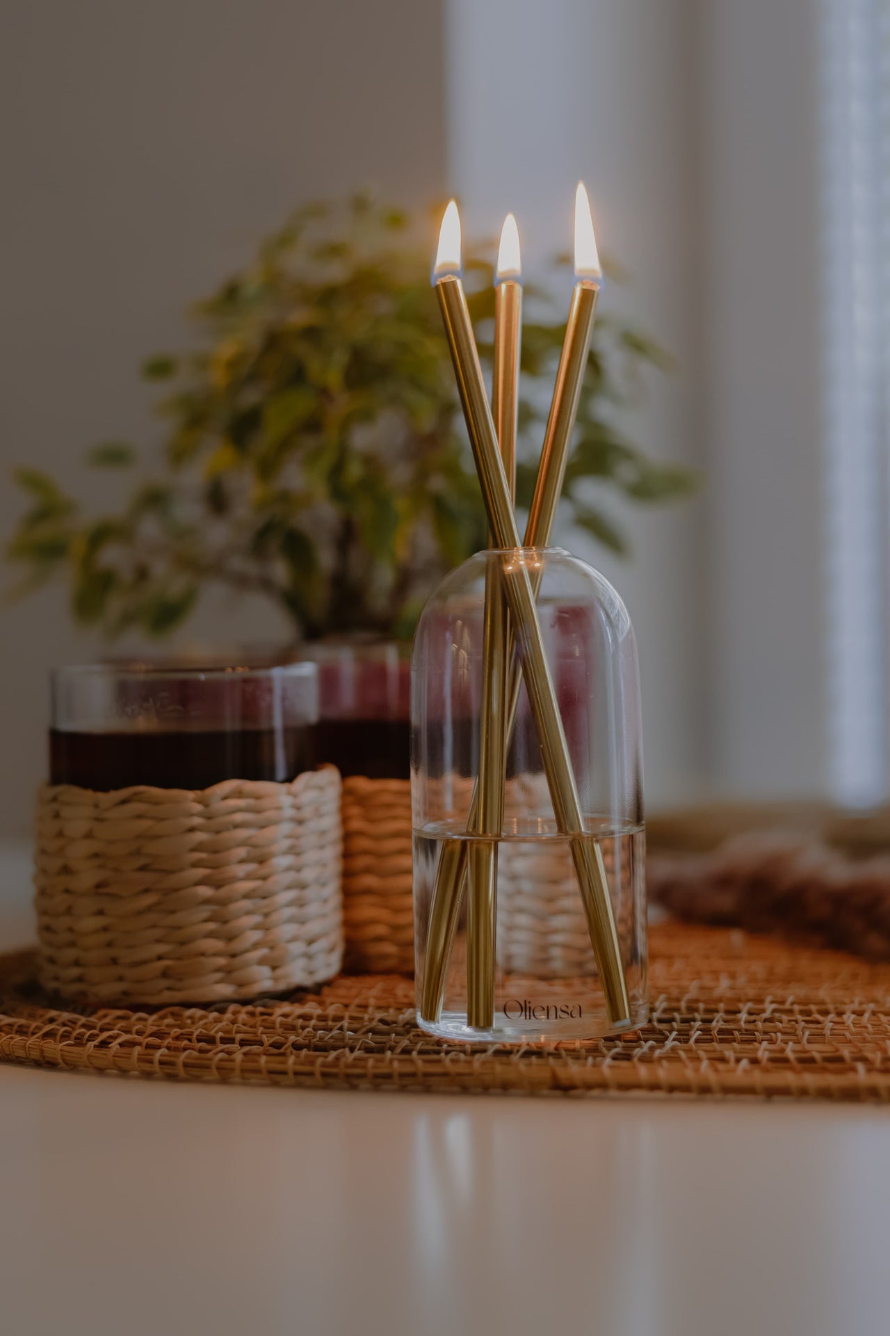 Świeca Oliensa Crystal Gold na stole w towarzystwie szklanek – subtelne światło i metaliczny połysk w eleganckiej, codziennej aranżacji.